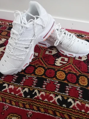 Nike Air Max Plus vita sneakers - Nike Air Max Plus sneakers i helvitt med detaljer i orange på sulan. Skorna har en sportig design med mesh- och syntetmaterial, synliga Air Max-enheter och robust yttersula. Perfekt för dig som gillar streetwear och vill ha en clean look.