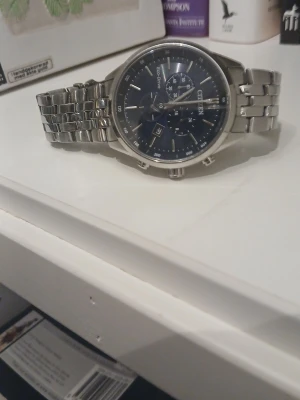 Citizen  - Citizen Eco-Drive klocka med mörkblå urtavla och silverfärgat armband i metall. Klockan har flera små urtavlor, datumvisning och klassisk länkdesign. Perfekt accessoar för dig som gillar en tidlös look. Se defekter på baksidan                Pendlar från Alingsås till Skövde vardagligen. Med jämna mellanrum är jag även i Uppsala. Säg gärna till om ni vill mötas och slippa betala frakten och den extra kostnaden som plick sätter på priset. Ni betalar med swish isåfall :) 