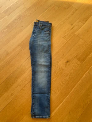 Blå slim fit jeans från Jack & Jones - Snygga blå slim fit jeans från Jack & Jones med klassisk femficksdesign och skinnpatch bak i midjan. Jeansen har en lätt tvättad look med slitningar på låren och smal passform. Perfekta för en avslappnad och trendig stil.