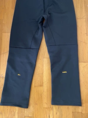 Svarta mjukisbyxor från Nike NOCTA - Svarta mjukisbyxor från Nike NOCTA med broderade detaljer i gult på benen. Byxorna har resår i midjan med dragsko och är tillverkade i mjukt material för maximal komfort. Perfekta för en avslappnad och trendig stil. KAN ÄVEN SÄLJA BYXORNA ENSKILT. KAN ÄVEN DUSKITERA PRIS