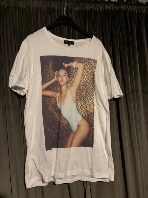 Vit t-shirt med leopardprint-tryck - Vit t-shirt från dead legacy med ett stort tryck framtill av en person i baddräkt mot leopardmönstrad bakgrund. Klassisk rund halsringning och korta ärmar. Perfekt statement-plagg för dig som gillar unika prints.