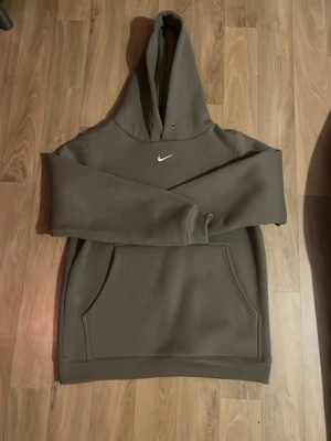 Nike hoodie  - Snygg brun hoodie från Nike med klassisk vit swoosh-logga på bröstet. Hoodien har stor huva med dragsko och en rymlig magficka framtill. Perfekt för en avslappnad streetwear-look. Tillverkad i mjukt och bekvämt material.
