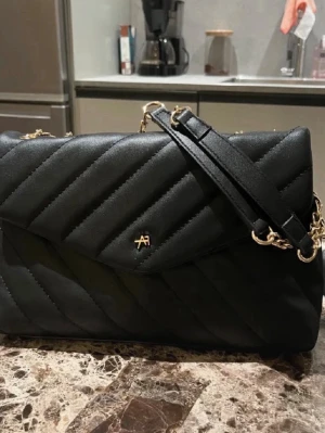  Anna field Väska - Snygg svart axelväska från Anna field i quiltat konstläder. Väskan har guldfärgade kedjedetaljer och justerbar axelrem. Stängs med lock och magnetknapp. Perfekt för dig som vill ha en stilren och trendig väska med plats för det viktigaste.