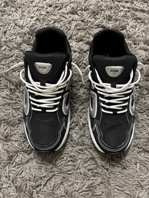 Svarta B30 sneakers med silverdetaljer - Snygga svarta  sneakers med vita och silverfärgade detaljer. Skorna har en chunky vit sula, mesh och syntetmaterial på ovandelen samt tydliga på sidorna. Vita skosnören och sportig design som sticker ut.