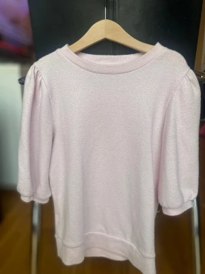 Ljusrosa topp från 157 med puffärm - Supersöt ljusrosa topp från 157 i mjukt material. Modellen har puffiga korta ärmar och rund halsringning. Perfekt för dig som gillar en feminin och enkel stil. Passar till både jeans och kjol.