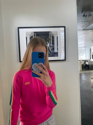 Rosa stickad tröja From Future - Snygg rosa stickad tröja från From Future med regnbågsfärgade ränder längs ärmarna. Tröjan har rund halsringning och en tightare passform. Perfekt för dig som vill sticka ut med färg och stil.