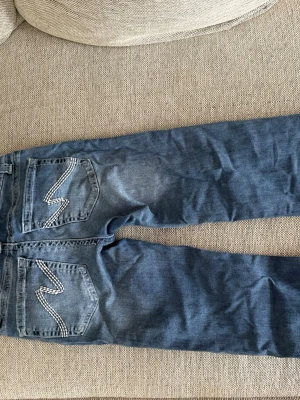 Blå jeans från Nelly - Säljer ett par blå jeans med slitningar på benen och cool broderad detalj på baksidan. Hålen är gjorda av den ja köpte av super fina i storlek 32