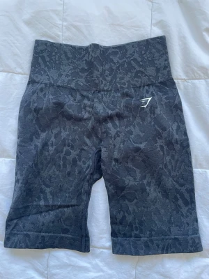 Mörkgrå seamless cykelshorts Gymshark - Säljer ett par mörkgrå seamless shorts från Gymshark med diskret ormmönster och scrunch. Hög midja och stretchigt material som sitter skönt vid träning. Gymshark-logga i vitt på vänster sida framtill. Perfekta för gymmet eller löprundan.