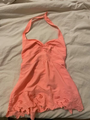  halterneck topp  - Supersöt korallfärgad halterneck topp från American Eagle Outfitters. Toppen har broderade spetsdetaljer nertill och en lätt v-ringad byst. Perfekt för varma dagar och ger en fräsch sommarkänsla.
