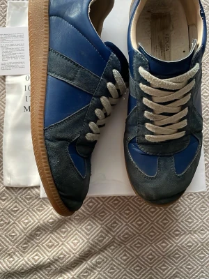 Maison margiela gats - Tja! Säljer dessa blåa Maison Margiela Replica sneakers i blått och mörkgrå mocka med vita snören och klassisk gummisula. Snygg retrostil med paneler i både läder och mocka. Perfekta för dig som gillar stilrena och unika sneakers med streetkänsla.