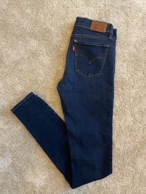Mörkblå skinny jeans från Levi's - Snygga mörkblå skinny jeans från Levi's med klassisk femficksdesign och gul kontrastsöm. Jeansen har en ikonisk läderpatch bak i midjan och röd Levi's-tag på bakfickan. Tillverkade i stretchigt denim för en bekväm passform.