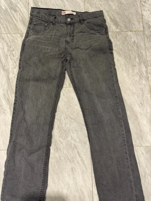Grå raka jeans från Levi's - Säljer ett par grå jeans från Levi's med klassisk femficksmodell och raka ben. Jeansen har en diskret tvätt och Levi's ikoniska röda etikett på bakfickan. Tillverkade i bomull med en skön passform som funkar till det mesta.