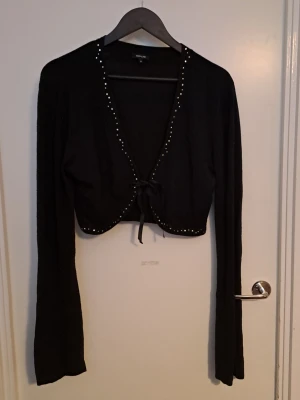 Svart bolero  - Svart boleto med långa ärmar och knytband framtill. Koftan har pärldetaljer längs kanten, det är som diamanter typ. Ärmarna är långa och utsvängda. 🩷