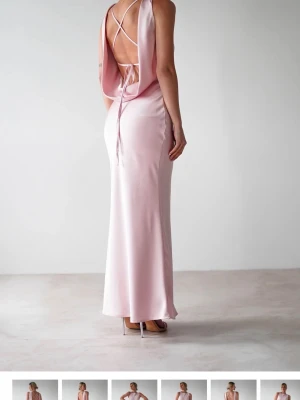 Ljusrosa balklänning i satin - Elegant ljusrosa långklänning i satin med öppen rygg och tunna korsade band. Klänningen har en draperad rygg och smal passform som ger en stilren siluett. Perfekt för dig som vill vara lite classy