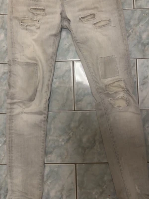 Ljusa ripped jeans från Dsquared2 - Säljer ett par ljusgrå slim fit jeans från Dsquared2 med slitningar och patchade detaljer på benen. Jeansen har klassisk femficksmodell och en snygg tvättad look. Perfekta för dig som gillar streetwear och vill sticka ut med coola detaljer.