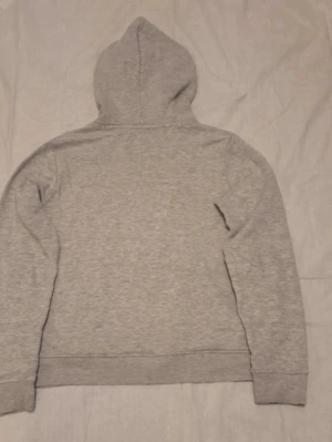 Ljusgrå hoodie med huva - En stilren ljusgrå hoodie med huva och långa ärmar. Tillverkad i mjukt sweatshirtmaterial, perfekt för en avslappnad look. Ribbstickade muddar vid ärmslut och nederkant. Klassisk passform utan synliga loggor eller tryck.