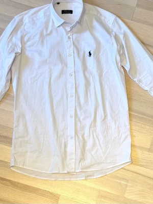 Vit skjorta från Polo Ralph Lauren - OBS, PRISET ÄR INTE SPIKAT SKRIV VID INTESSE! Endast använd 2 gånger! Klassisk vit skjorta från Polo Ralph Lauren med broderad logga på bröstet. Skjortan har lång ärm, knappar framtill och en tidlös krage. Perfekt för en clean och stilren look.