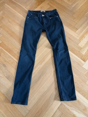 Mörkblå slim fit jeans - Snygga mörkblå slim fit jeans med klassisk femficksdesign och silverfärgade nitar. Jeansen har raka ben och normal midja, tillverkade i ett mjukt denimtyg som ger en skön passform. Perfekta för dig som gillar en stilren och Grish look. Storlek: 30/32