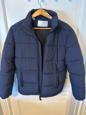 Mörkblå pufferjacka från Selected Homme - Snygg mörkblå pufferjacka från Selected Homme med hög krage och dragkedja framtill. Jackan har två sidofickor med dragkedja och quiltad design. Perfekt för kalla dagar och ger en clean look till din outfit. Skicka gärna prisförslag 