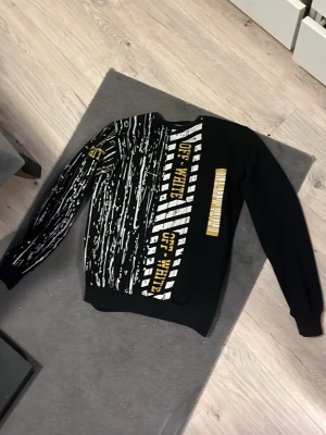 Svart Off-White sweatshirt med tryck - Säljer en svart sweatshirt från Off-White med unikt vitt och gult grafiskt tryck på både fram- och baksida samt ena ärmen. Tröjan har rund hals och ribbade muddar. Perfekt för dig som gillar streetwear och vill sticka ut med cool design.