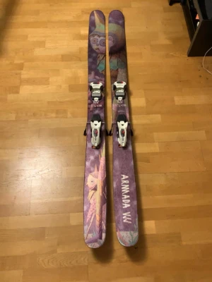 Armada VJJ skidor med bindningar - Säljer ett par Armada VJJ skidor med färgstarkt och unikt grafiskt mönster i lila, rosa och grönt. Skidorna har vita bindningar från Marker och är breda, perfekta för puderåkning. Grym design som sticker ut i backen! Nästan i helt perfekt skick