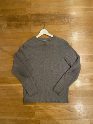 Grå stickad tröja från Zara - Säljer en enkel och stilren grå stickad tröja från Zara i storlek S. Tröjan har rund hals, ribbade muddar vid ärmslut och nederkant samt långärmad passform. Perfekt för dig som gillar en clean look och vill ha något som funkar till jeans.