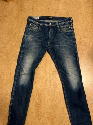 Replay Anbass jeans blå slim fit - Snygga blå Replay Anbass jeans i slim fit med klassisk femficksdesign och slitna detaljer på låren och knäna. Jeansen har normal midja och raka ben, tillverkade i mjukt och slitstarkt bomullsmaterial med lite stretch för extra komfort.