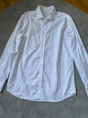 Vit skjorta från Massimo Dutti - Klassisk vit skjorta från Massimo Dutti med krage och knappar hela vägen framtill. Skjortan är långärmad och tillverkad i mjuk bomull. Perfekt för dig som gillar stilrena och enkla plagg med snygg passform. Skjortan är använd 1 gång och därmed är som näst in till ny.