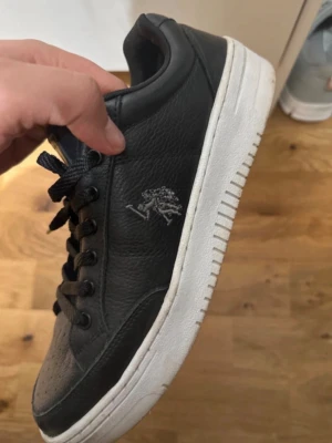 Äkta läder  - Säljer ett par svarta sneakers från U.S POLO ASSN med vit platt sula och snörning. Skorna är gjorda i skinn och har POLO klassiska trädlogga broderad på sidan. Perforerad tå och rund form ger en clean och sportig vibe.