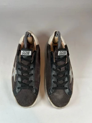 Golden goose - Säljer ett par Golden goose sneakers i svart mocka och skinn med vit stjärndetalj på sidan och vit häl. Klassisk låg modell med svarta skosnören och slitna detaljer för en cool vintage-look. Sulan är vit med svarta partier undertill.