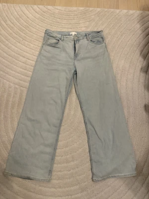 Ljusblå wide jeans från H&M - Säljer ett par ljusblå jeans från H&M i storlek 44. Modellen har breda ben och klassisk femficksdesign med knapp och dragkedja framtill. Jeansen är tillverkade i bomull och har en avslappnad, modern vibe som passar perfekt till sneakers.