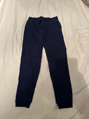 Mörkblå mjukisbyxor Basic You - Mörkblå mjukisbyxor från Basic You i ekologisk bomull. Byxorna har ribbade muddar vid bensluten och en elastisk midja med snörning. Perfekta för chill eller träning, med skön passform och mjukt material.