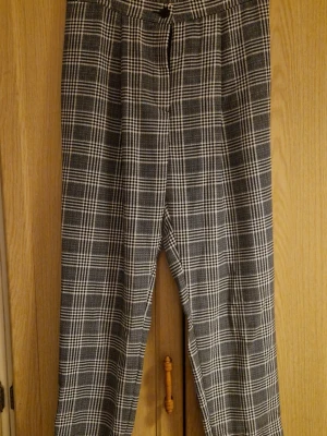 Rutig byxa från Divided, storlek 40 - Snygga svartvitrutiga byxor från Divided i storlek 40. Byxorna har en rak passform och är gjorda i 100% polyester. De har klassiskt rutmönster och midja med knapp och dragkedja framtill. Perfekt för dig som gillar stilrena och trendiga mönster. Kolla gärna in mina andra annonser! 
