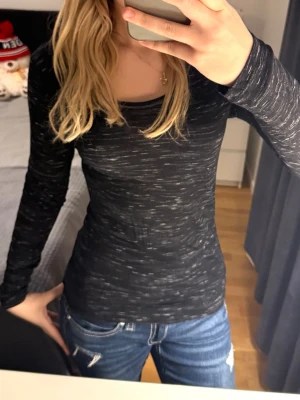 Svart långärmad topp med mönster - Svart långärmad topp från Noisy May med tunna vita streck som ger ett randigt intryck. Modellen är figurnära med rund halsringning och stretchigt material som känns skönt mot huden. Perfekt att styla med jeans eller kjol.