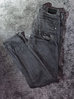 **Unika** Replay Anbass  - Unika Svarta jeans från Replay med läderpatch på bakfickan och snygga dragkedjedetaljer vid fickorna. Klassisk femficksmodell med smal passform och låg midja. Materialet är jeans med en mjuk känsla och stretch för extra komfort. Perfekt för dig som gillar en stilren och modern look. Ända sättet att stå ut med replay är dessa;)