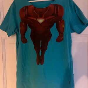 Turkos Marvel Iron Man t-shirt XL - Säljer en turkos t-shirt från Marvel i storlek XL med en stor Iron Man-tryck på framsidan. T-shirten är gjord i 100% bomull och har korta ärmar. Perfekt för dig som gillar superhjältar och vill sticka ut med en cool design. Kragen är klippt.