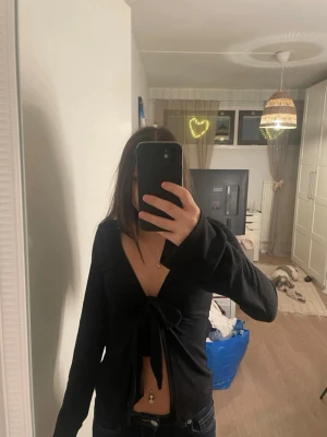Svart omlottopp med knyt från Gina Tricot - Säljer en svart omlottopp från Gina Tricot i storlek XS. Toppen har lång ärm, djup v-ringning och en snygg knytning framtill som ger en croppad look. Perfekt att styla med jeans eller kjol för en trendig outfit.