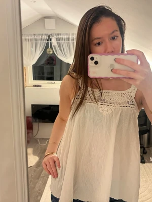 Vit linnetopp med virkade detaljer - Supersöt vit linnetopp med virkade detaljer upptill och breda axelband. Toppen är ärmlös och har en luftig, flowy passform. Perfekt för varma dagar och ger en bohemisk vibe. Materialet känns lätt och toppen har en fin struktur. Obs det står ingen storlek men passar som xs-s!