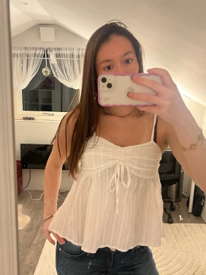 Vit linnetopp med knyt fram - Superfin vit linnetopp med tunna axelband och söt knytning framtill, som är köpt i thailand. Toppen har en lätt rynkad struktur och faller luftigt, perfekt för varma dagar. Materialet känns svalt och toppen har en feminin, flowy look. Obs det står ingen storlek men passar som xxs-xs!