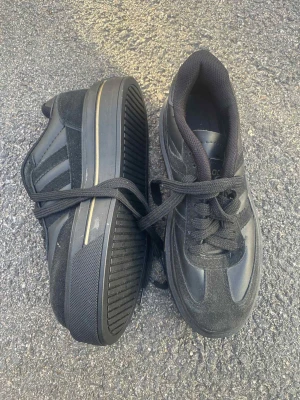 Svarta Adidas sneakers med guldiga detaljer - Säljer ett par svarta Adidas sneakers med guldiga loggor och detaljer. Skorna har platt sula, snörning och är tillverkade i en mix av mocka och syntetmaterial. Klassisk Adidas-design med tre ränder på sidan och guldtryck på hälen.