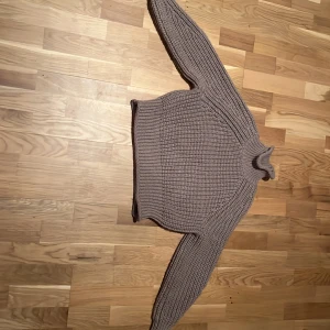 Beige stickad polotröja från H&M - Säljer en chunky stickad polotröja i beige med grov ribbstickning. Tröjan har hög krage och långa ärmar med breda muddar. Perfekt för kyliga dagar och superenkel att styla med jeans eller kjol. Har knappt använt.