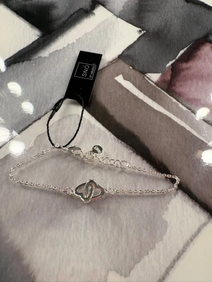 Säljer inget västplagg - Säljer ett armband från Snö of Sweden i silverfärg med två sammanlänkade hjärtan. Oanvänt med lapp kvar. 
