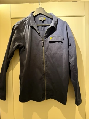 Mörkblå overshirt från Lyle & Scott - Snygg mörkblå overshirt från Lyle & Scott med klassisk krage och dragkedja framtill. Bredd 40 Läbgd 60