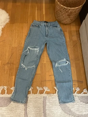 Blå ripped jeans från ASOS DESIGN - Säljer ett par ljusblå jeans från ASOS DESIGN  med stora ripped detaljer på båda benen. Högmidjade och raka i modellen, tillverkade i klassisk denim. Perfekta för dig som gillar en avslappnad och trendig stil.