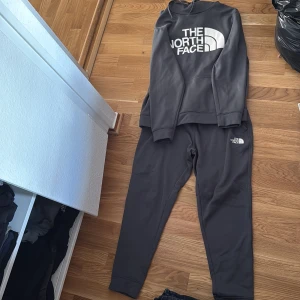 Svart hoodie från The North Face och byxor - Säljer en svart hoodie från The North Face med stor vit logga på bröstet. Tröjan har lång ärm, klassisk huva och är gjord i mjukt material som passar perfekt till chill eller träning. Snygg och enkel stil som funkar året runt. Och byxorna till