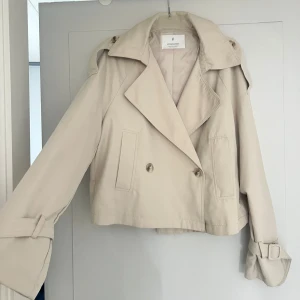 Beige trenchcoat från Stradivarius - Croppad trenchcoat i beige från Stradivarius.