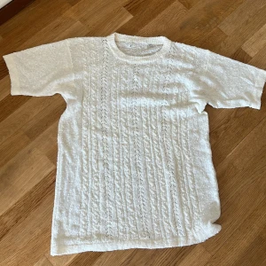 Vit stickad kortärmad tröja med pärlor - Supersöt vit stickad tröja med korta ärmar och rund hals. Tröjan har ett detaljerat flätmönster och är dekorerad med små pärlor på framsidan (se bild 2).