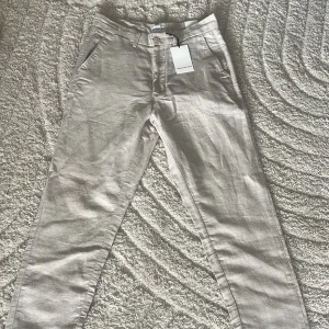 Beige linnebyxor från These Glory Days - Snygga och stilrena beige linnebyxor från These Glory Days. Byxorna har klassisk passform med raka ben, hällor för bälte och sidfickor. Perfekta för en chill och fräsch look under varmare dagar. Materialet är lätt och andas bra. Väldigt sköna och lätta till våren/sommaren.