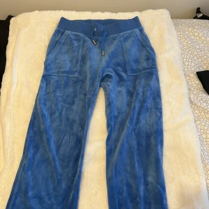 Blå mjukisbyxor i velour - Byxorna är i XS och koftan är i S. Kedjan till koftan har gått sönder. Blå mjukisbyxor i mjuk velour med bred resår i midjan och snörning. Byxorna har stora fickor fram och bakfickor med knappar. Perfekta för chill dagar och har en riktigt skön loose fit.