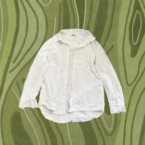 Vit skjorta från JDY i bomull - Klassisk vit skjorta från JDY i storlek 42. Skjortan har lång ärm, knappar framtill och en tidlös krage. Tillverkad i mjuk bomull och passar perfekt till jeans eller kjol för en clean look. Har en liten markering på armen från en penna men det syns knappt.